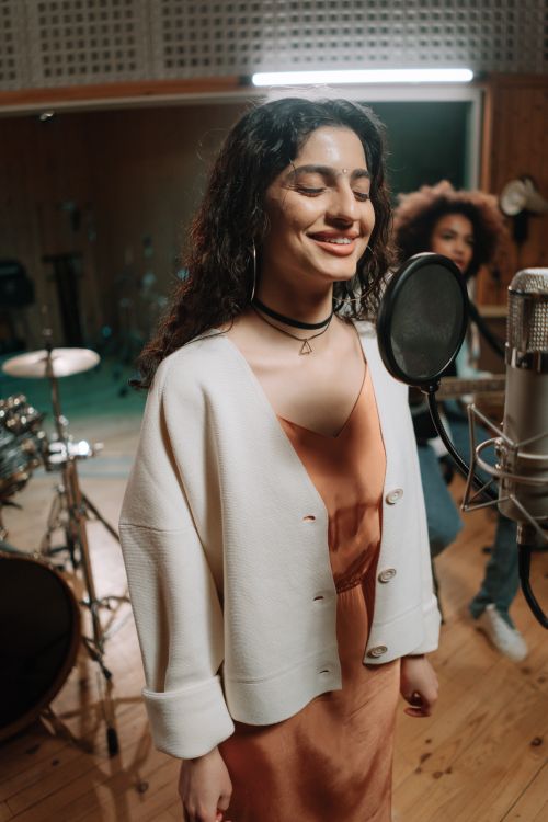 Free A woman joyfully sings into a condenser microphone in a cozy music studio setting. Stock Photo