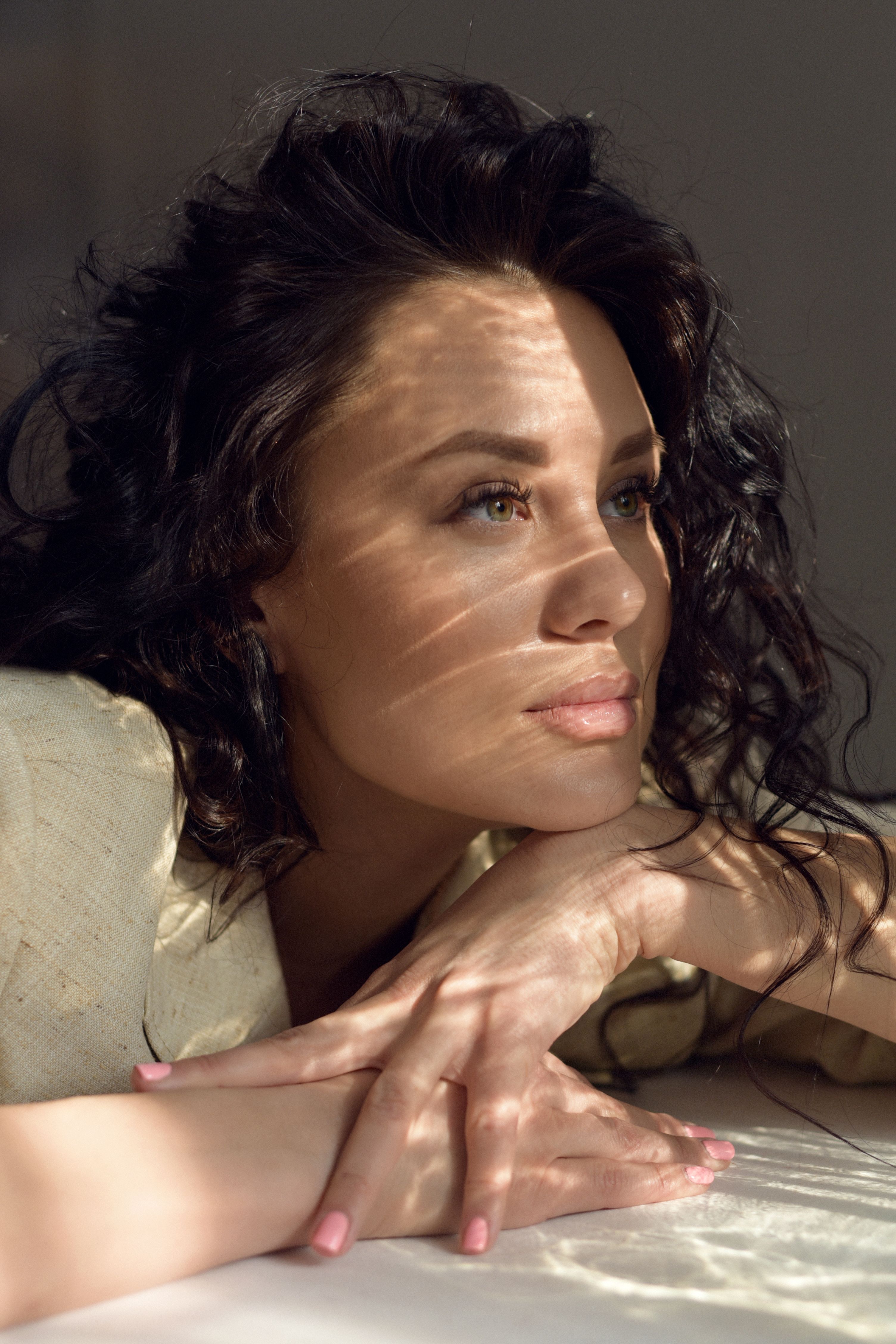 Close-up portrait capturing a woman's serene expression as sunlight filters through blinds onto her face.