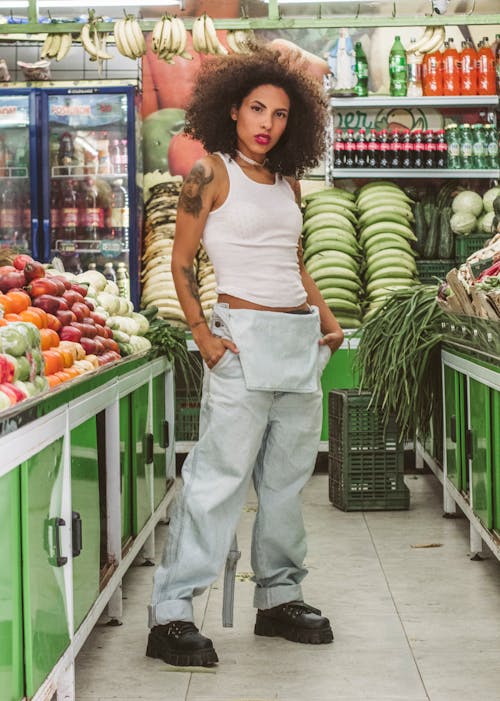 A Woman in Denim Overalls Standing Near a Vegetable Stand