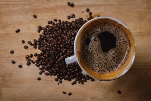 Close-up of a steaming cup of black coffee with scattered coffee beans on wooden background.
