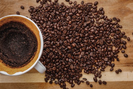 Close-up of fresh coffee beans scattered next to a brewed cup on a wooden surface.