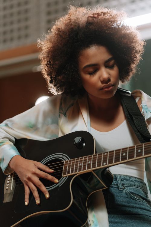 Free An African American woman focuses as she plays acoustic guitar indoors. Stock Photo