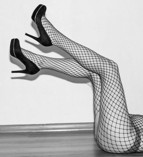 Free Artistic monochrome photo of legs in fishnet stockings and high heels, lying on a wooden floor. Stock Photo