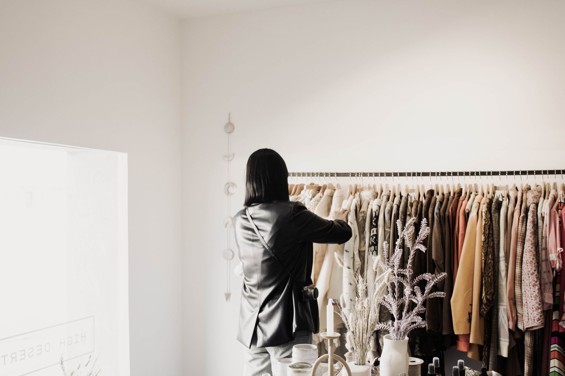 A woman browsing jackets in a stylish boutique with natural lighting and elegant decor.