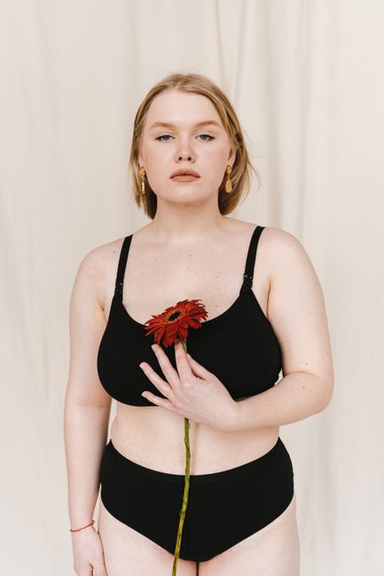 A confident woman in swimwear holding a gerbera daisy in a studio setting.