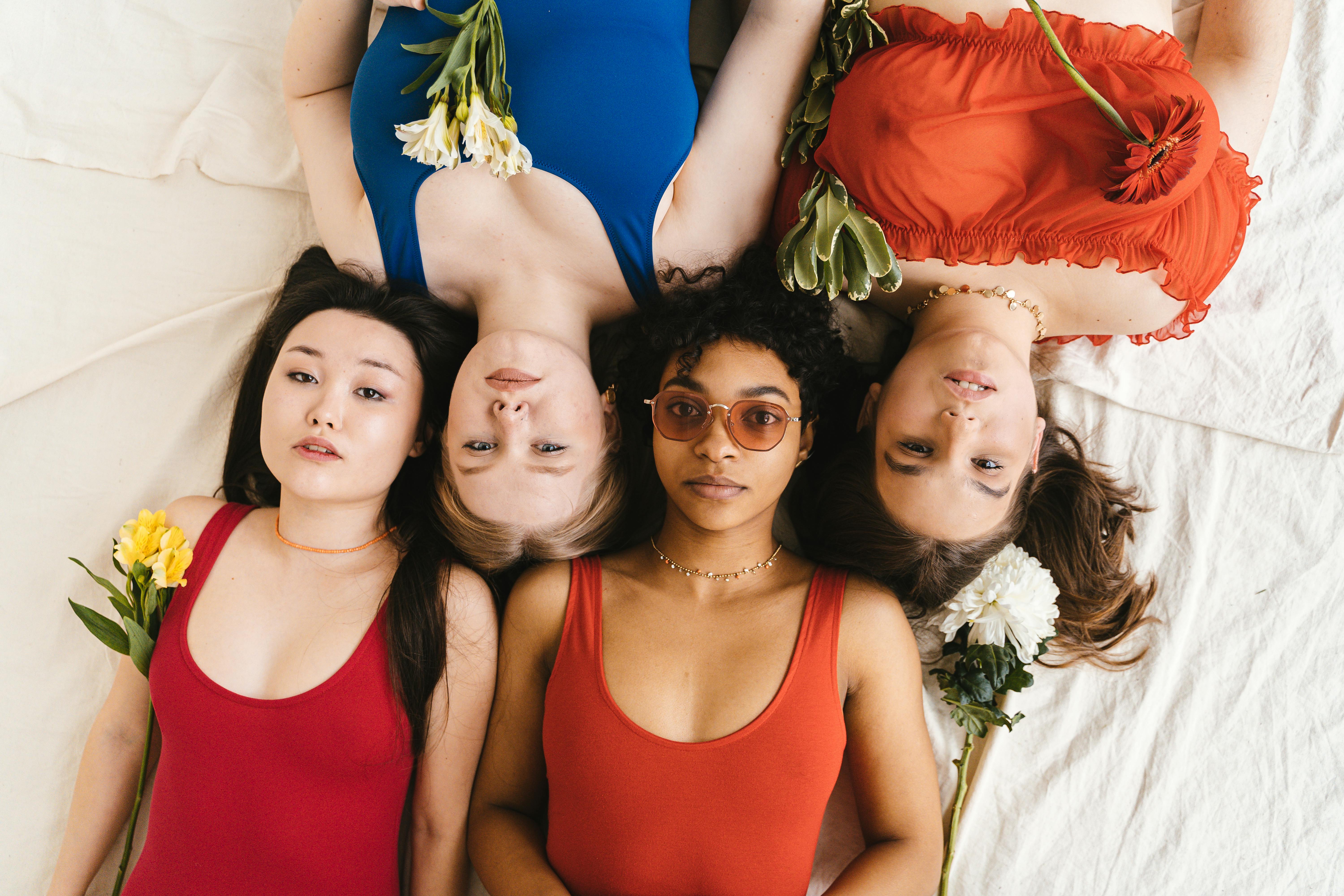 Four diverse women in vibrant swimwear with flowers, highlighting unity and femininity.