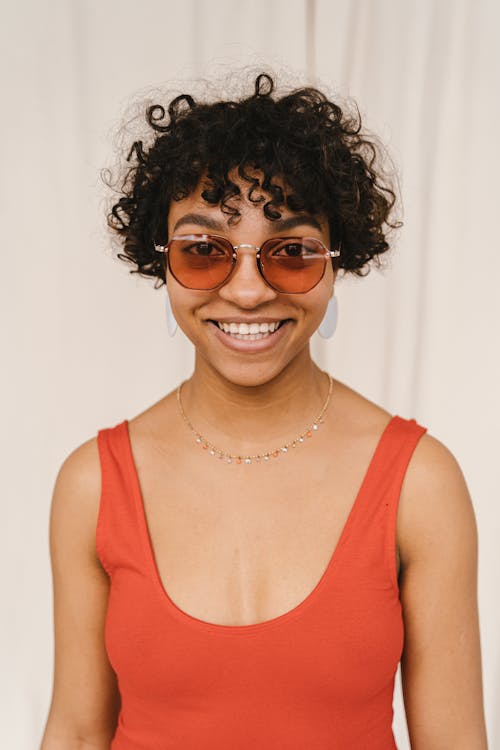 A Woman in Orange Tank Top Smiling while Wearing Sunglasses