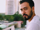 阳台上站着一位留着胡须、表情严肃的男子，背景是模糊的城市建筑