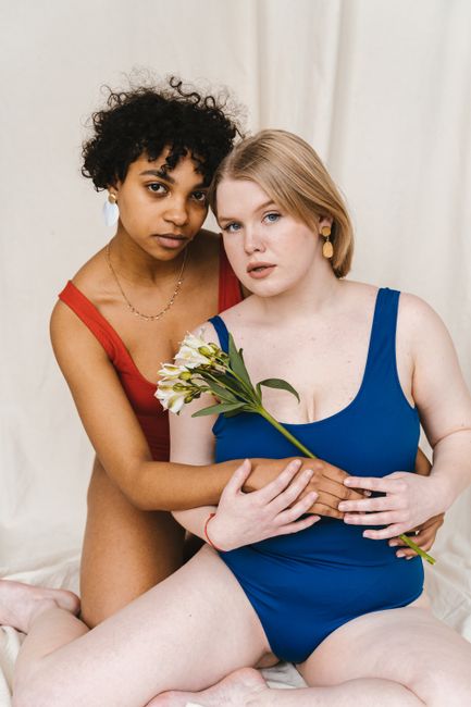 Two women in swimsuits embracing with flowers, celebrating diversity.