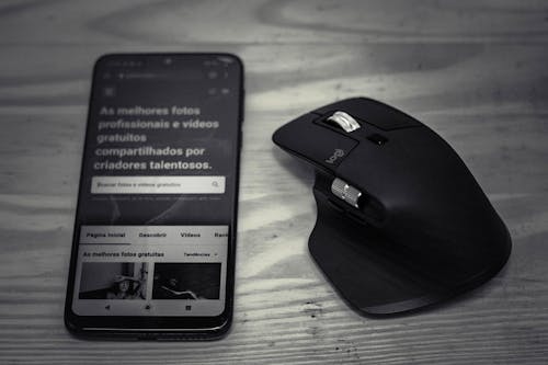 From above of mobile phone with information near modern computer mouse on wooden table