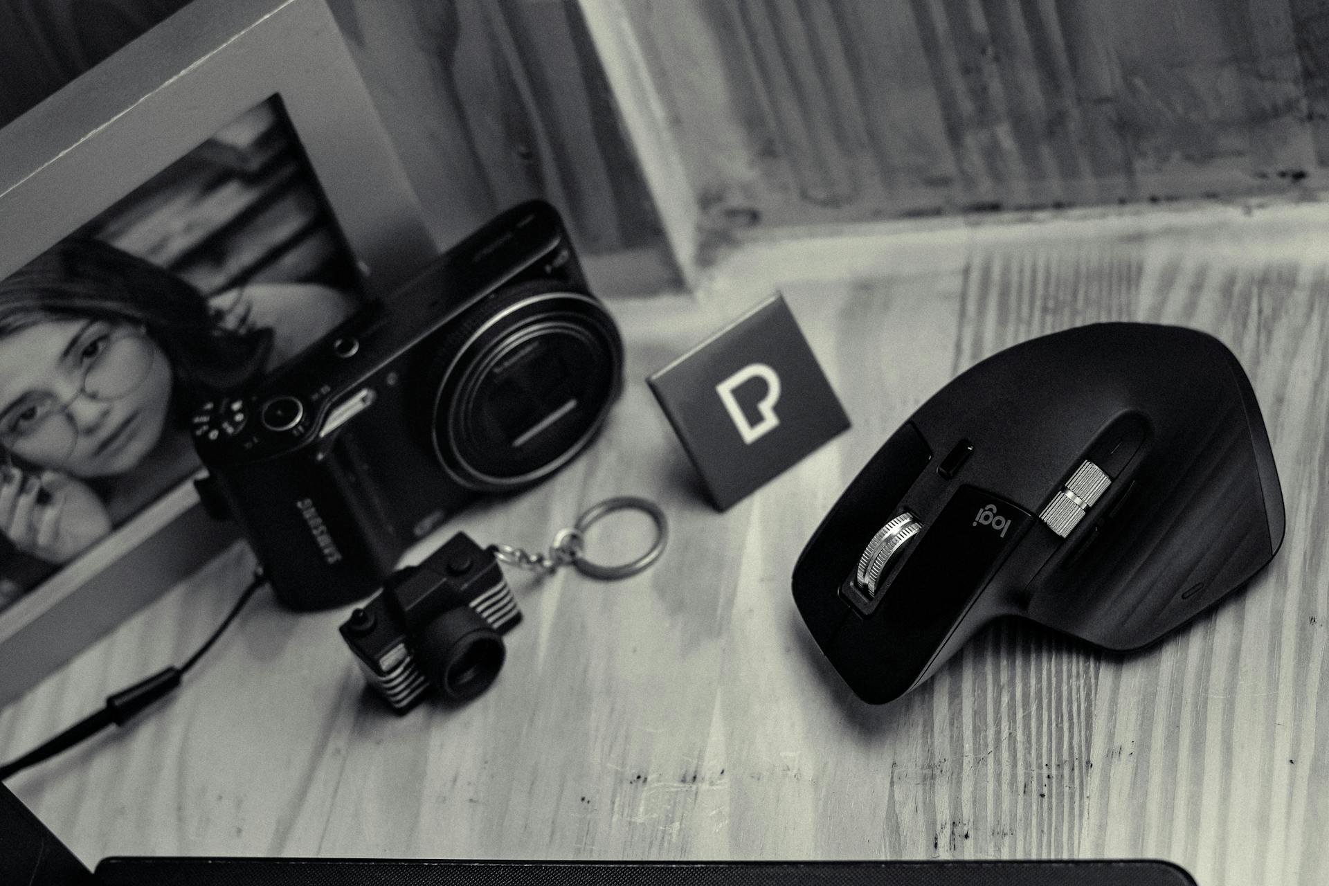 Monochrome desk setup featuring a camera, computer mouse, and framed photo, showcasing modern technology.