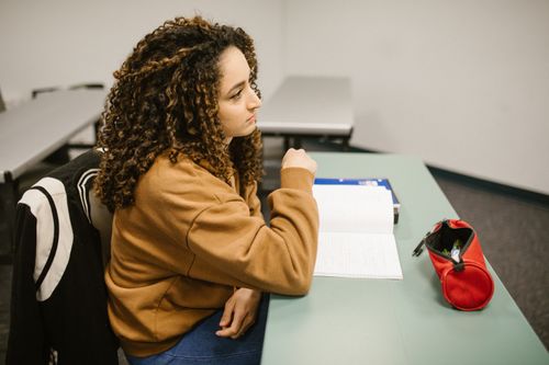 Free A university student sitting at a desk, pondering over notes in a classroom setting. Stock Photo