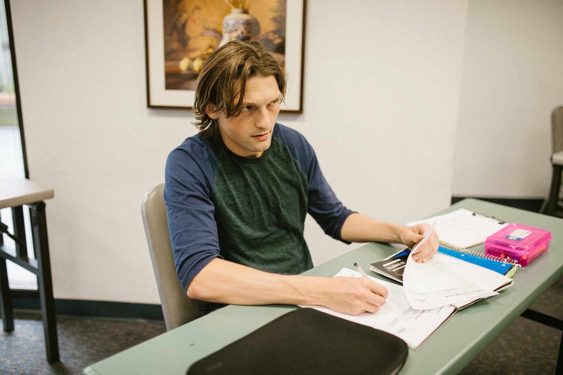 A male college student is sitting at a desk focusing on his studies in a classroom setting.