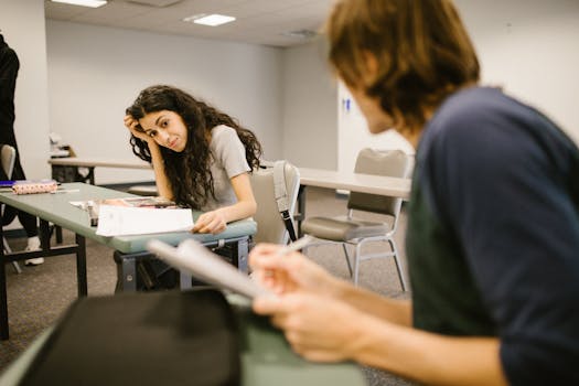Two college students engaged in discussion in a classroom setting, focusing on study material.