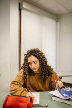 Woman preparing for exam in a classroom, writing notes with focus.