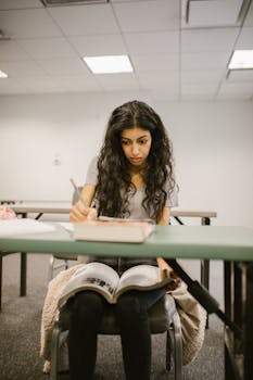 Focused college student writing notes with open book in classroom setting.