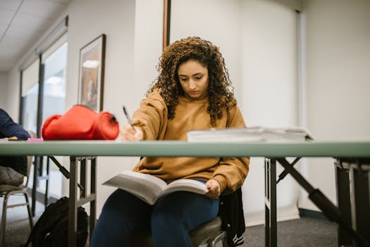 A student absorbed in study, writing notes in a classroom setting.