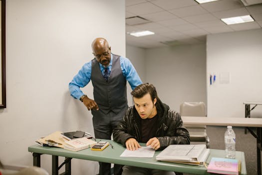 A teacher reprimands a student caught cheating in a classroom with study materials on the desk.