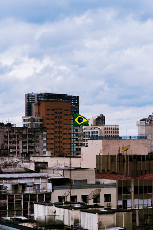 Free Dramatic view of São Paulo skyline featuring a prominent Brazilian flag under a cloudy sky. Stock Photo