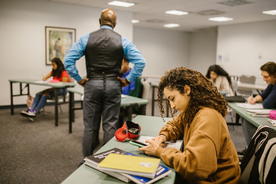 Students in a classroom setting with a teacher proctoring. Educational environment.