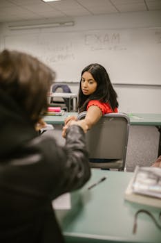Two students subtly exchanging notes during an exam in a classroom setting.