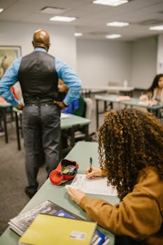 College students taking a test in a classroom setting with a teacher supervising.