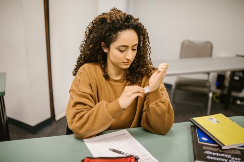 Free Female student discreetly checking a cheat sheet on arm during an exam in a classroom setting. Stock Photo