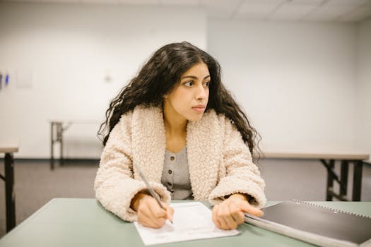 A college student writing on a test paper while looking away in a classroom setting.