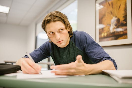 Male college student looking away with a cheat sheet during an exam in a classroom setting.