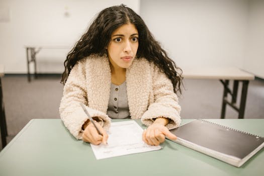 Concentrated woman writing an exam in a classroom setting, showcasing study focus.
