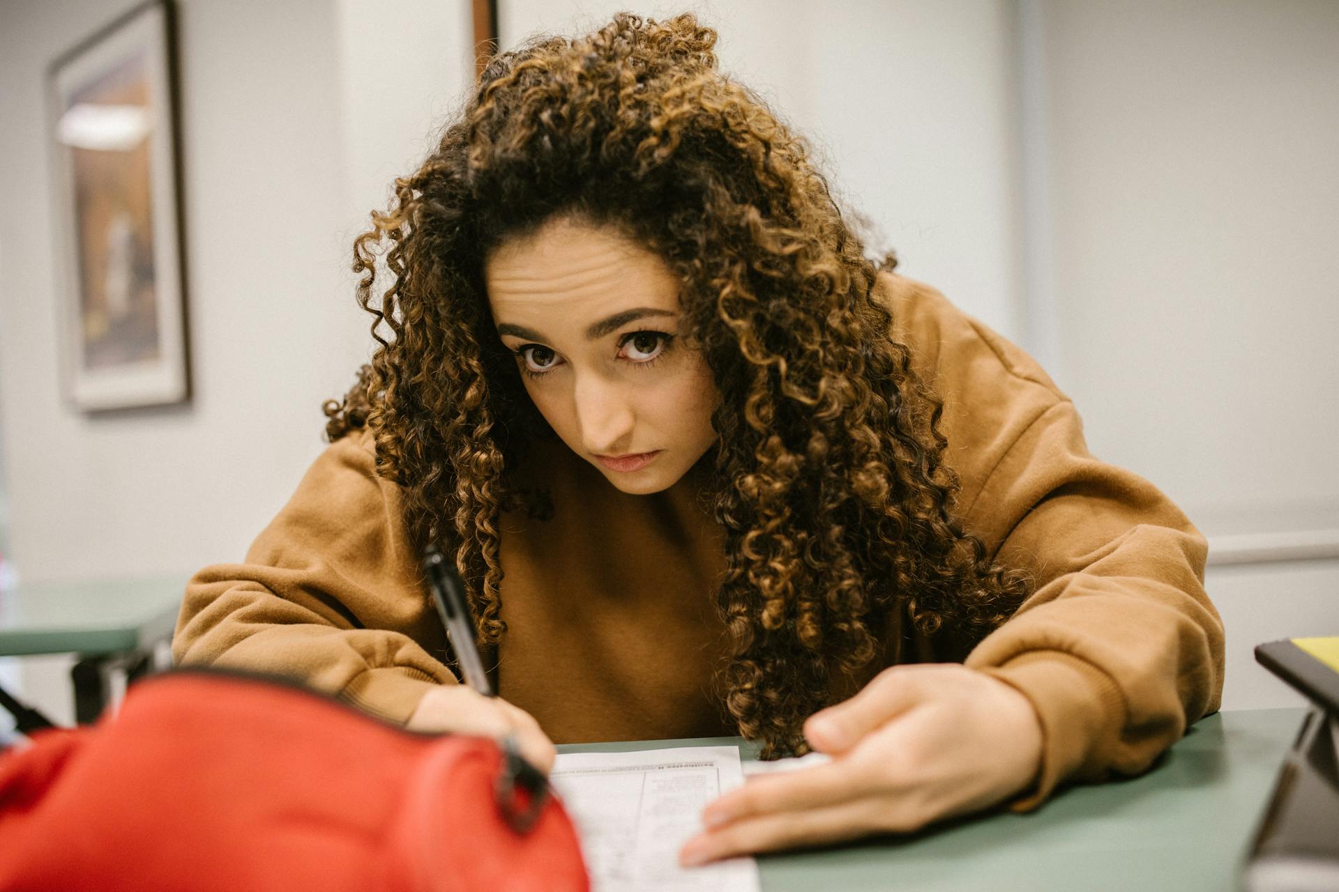 Female student deeply engaged in exam writing in a classroom setting.