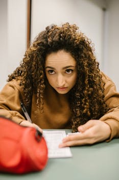 A focused female student writing on a test paper during an exam in a classroom setting.