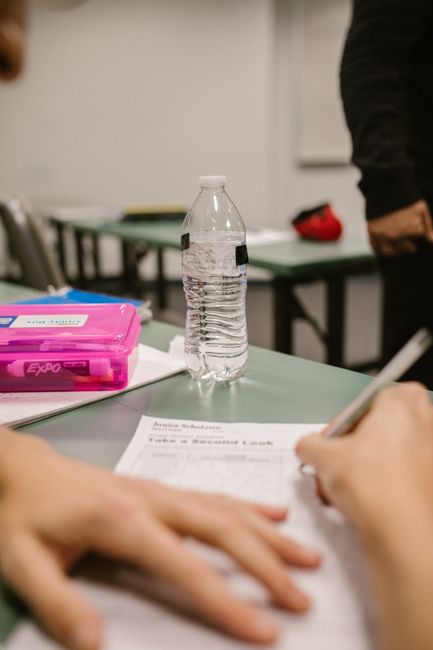Close-up of a student writing during a test in a classroom setting with a water bottle on the desk.