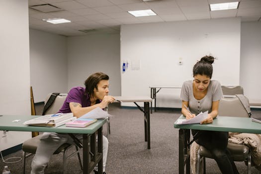 Two college students in a classroom setting, one appears to be copying from the other's paper.