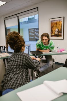 Two college students engaged in a conversation while studying in a classroom setting.