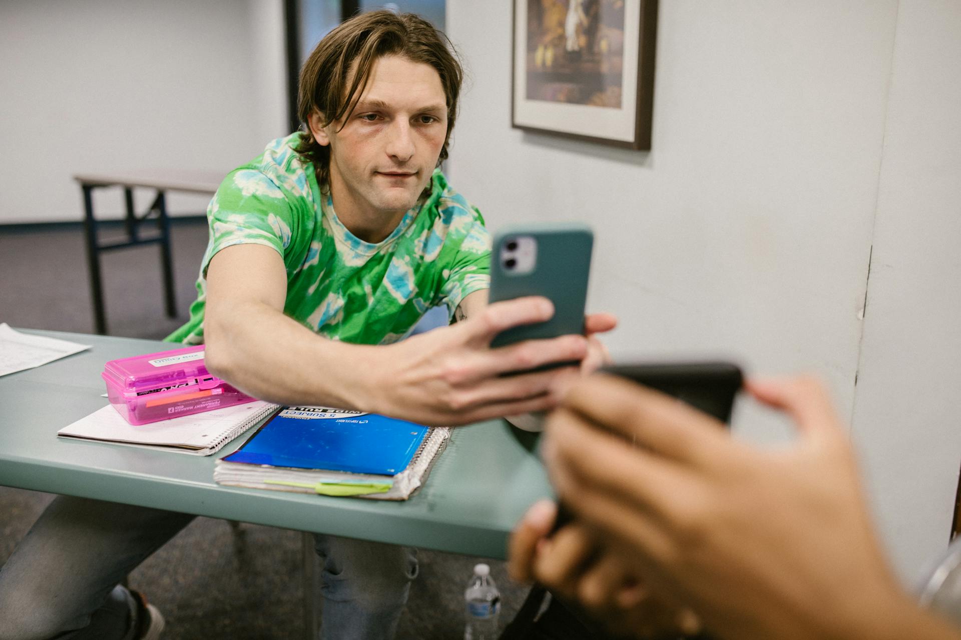 A student sharing his phone screen with another in a classroom setting.