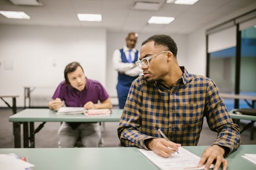Students in a classroom setting with a teacher observing during a test. Educational scene with diverse individuals.