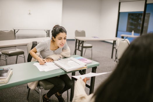 A female student in a classroom reviewing exam paper with a classmate, highlighting study collaboration.