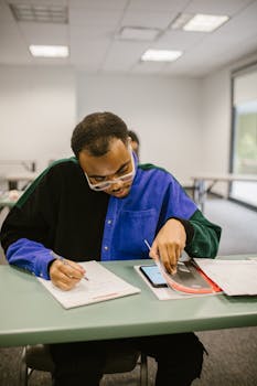 A student uses a smartphone and notes in a classroom to study or perhaps cheat.