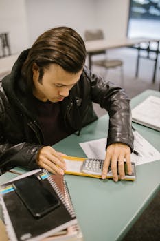 Young male college student using a calculator to solve a test paper in a classroom setting.