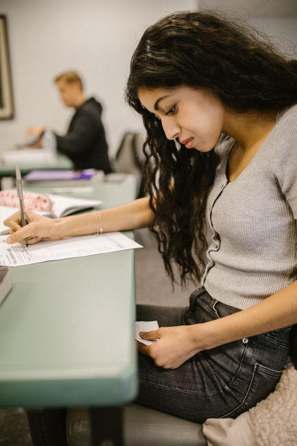 Student in classroom looking at notes while taking a test, hinting at cheating.