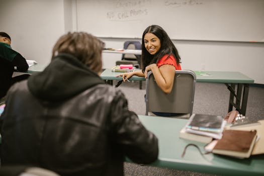 Students chatting during a break in a college classroom, surrounded by study materials and friendly atmosphere.