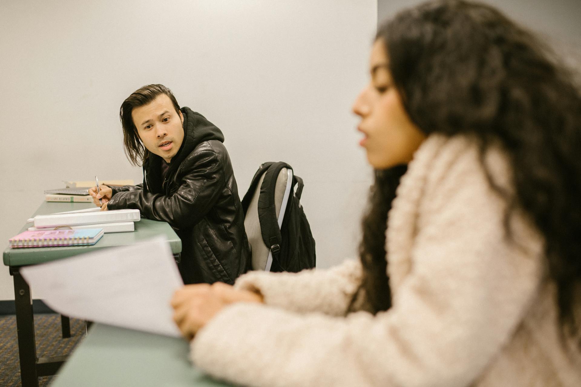 Two college students engaged in conversation during an exam in a classroom setting.