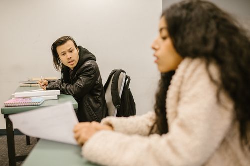 Free Two college students engaged in conversation during an exam in a classroom setting. Stock Photo