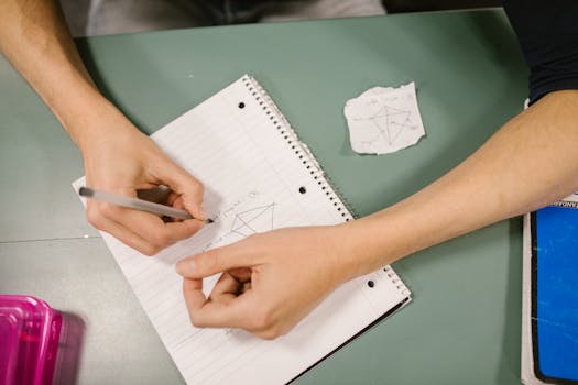 Close-up of a student writing notes during a college classroom session with study materials.