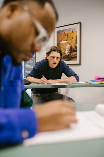 A student glancing at another student's paper, depicting cheating in a college classroom setting. A student glancing at another student's paper, depicting cheating in a college classroom setting.