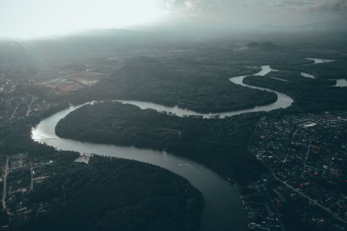 Free Drone view of curving river flowing through coasts covered with dense woods under sunlight shining through clouds Stock Photo