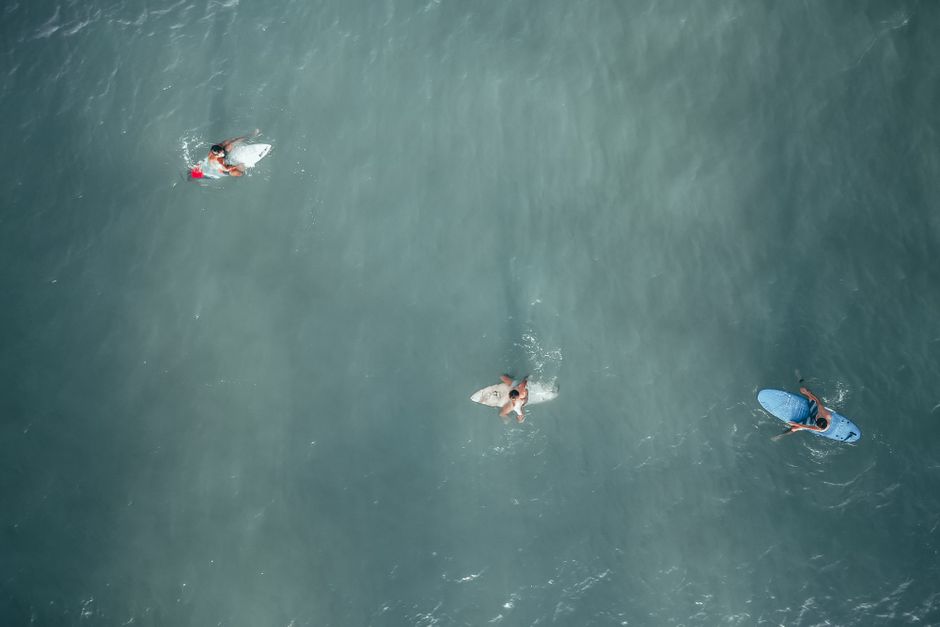 Drone view of surfers sitting on surfing boards in calm water of ocean on sunny day