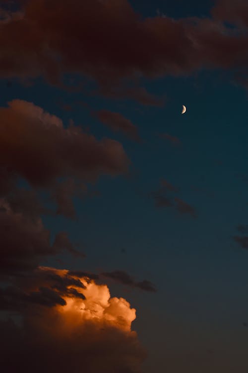 From below of moon in dark evening sky with cumulus clouds at sunset
