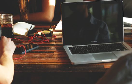 A cozy workspace featuring a MacBook Pro on a wooden table with a smartphone and drink, capturing relaxed technology use.